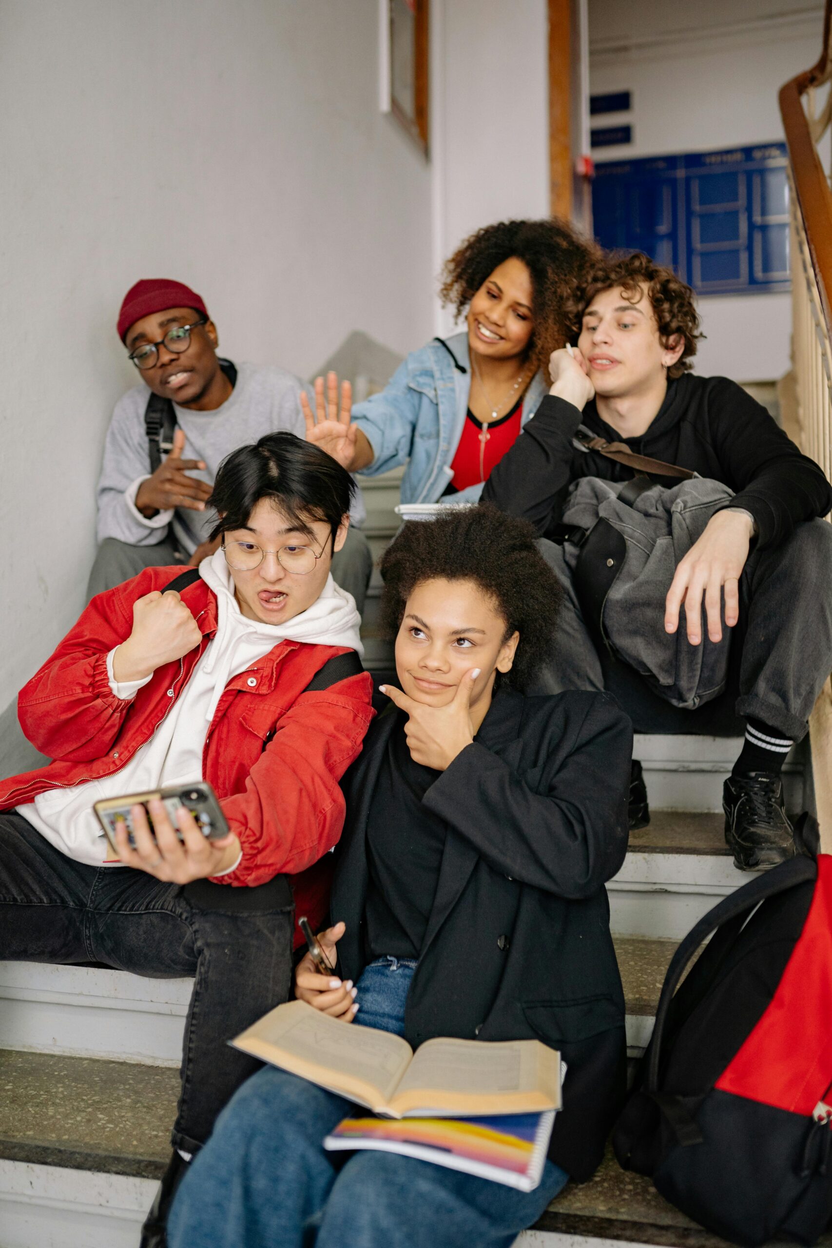 A diverse group of students posing together on stairs, taking a selfie indoors.