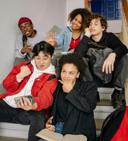 pexels-photo-8199201-8199201 A diverse group of students posing together on stairs, taking a selfie indoors.